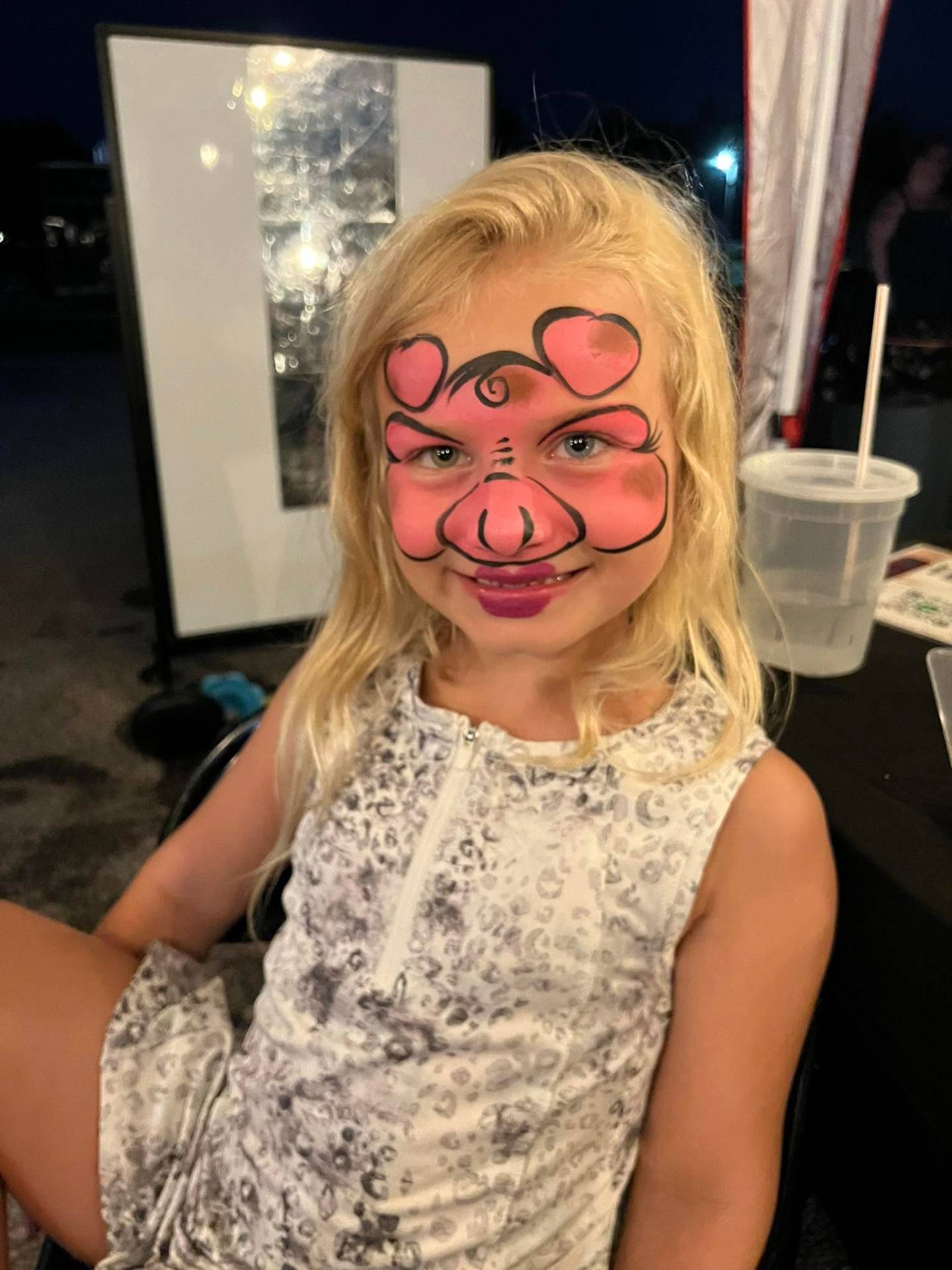Pink pig face paint design on a smiling child at a party