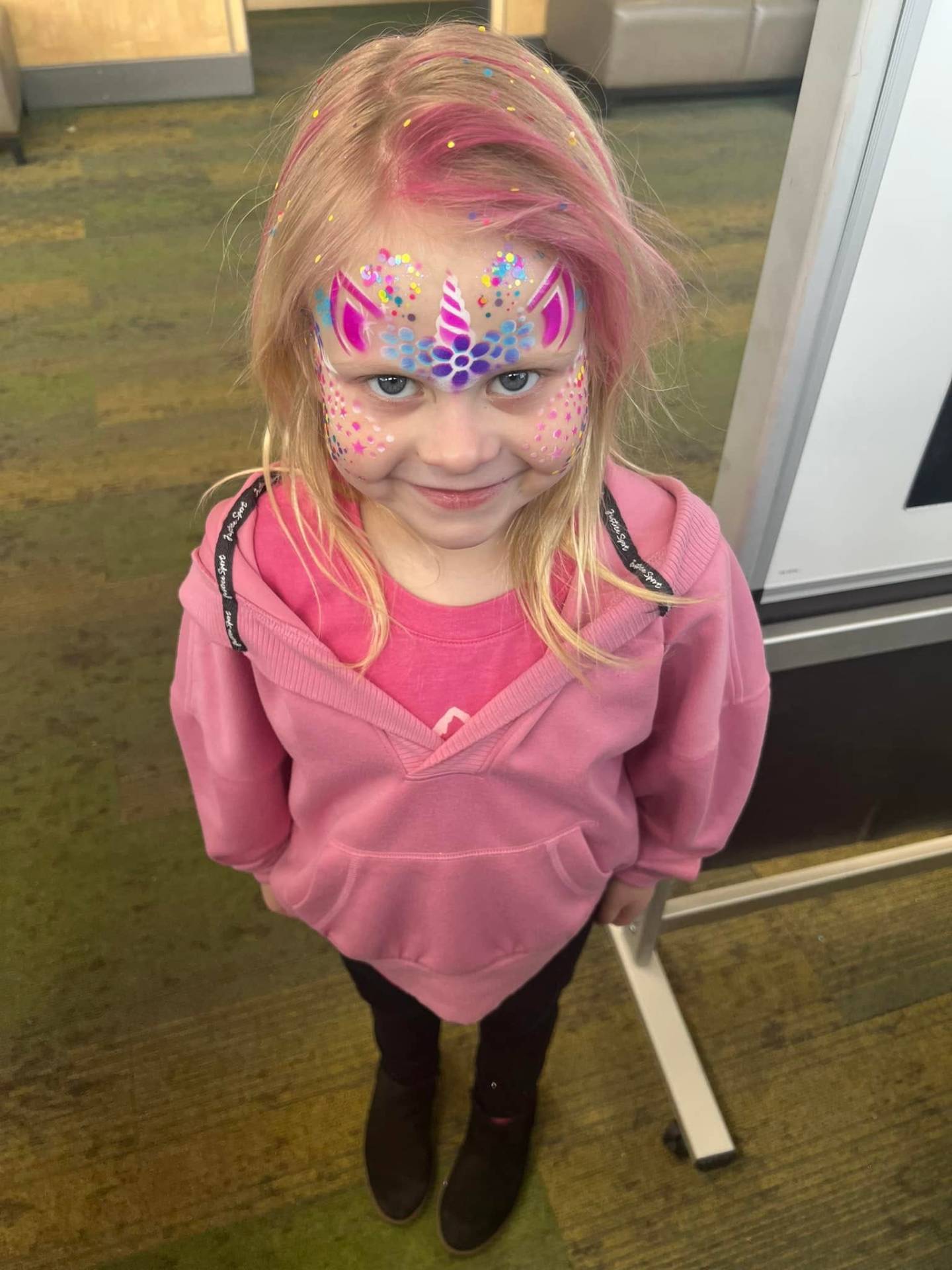 Pastel pink and purple unicorn face paint with glitter accents on a young girl at a birthday party